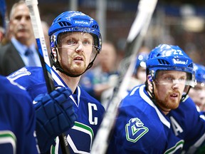 Daniel Sedin #22 and Henrik Sedin #33 of the Vancouver Canucks look on from the bench during their NHL game against the Edmonton Oilers at Rogers Arena April 11, 2015 in Vancouver, British Columbia, Canada.