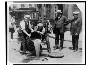 New York City Deputy Police Commissioner John A. Leach (right) watches agents pour liquor into the sewer following a raid, ca. 1921.