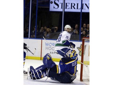 St. Louis Blues goalie Brian Elliott, bottom, keeps his eye on the puck after deflecting a shot from Vancouver Canucks' Chris Higgins (20) during the first period of an NHL hockey game Friday, March 25, 2016, in St. Louis. (AP Photo/Jeff Roberson)