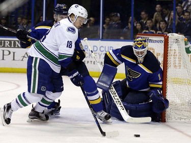 Vancouver Canucks' Jake Virtanen, left, controls the puck as St. Louis Blues goalie Brian Elliott defends during the first period of an NHL hockey game Friday, March 25, 2016, in St. Louis. (AP Photo/Jeff Roberson)