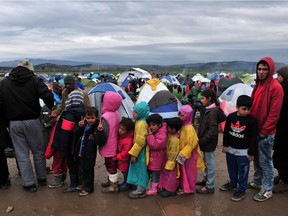 A young boy gestures as people wait in line to receive food near tents set up at the Greek-Macedonian border near the Greek village of Idomeni, where thousands of refugees and migrants are trapped by the Balkan border blockade, on March 9, 2016.  The main migrant trail from Greece to northern Europe was blocked on March 9 after western Balkan nations slammed shut their borders, hiking pressure for an EU-Turkey deal and exacerbating a dire situation on the Macedonian border.