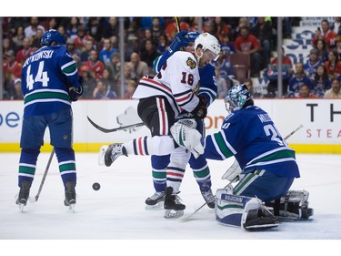 Chicago Blackhawks' Andrew Ladd (16) is struck by the puck while being checked by Vancouver Canucks' Alex Biega (obscured) in front of goalie Ryan Miller during the first period of an NHL hockey game in Vancouver, B.C., on Sunday March 27, 2016.