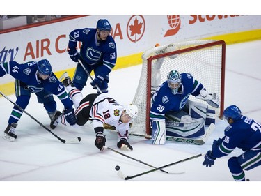Chicago Blackhawks' Tomas Fleischmann (12), of the Czech Republic, dives between Vancouver Canucks' Matt Bartkowski (44) and Bo Horvat (53) as he tries to get to the puck in front of goalie Ryan Miller (30) as Emerson Etem, right, defends during the second period of an NHL hockey game in Vancouver, B.C., on Sunday March 27, 2016.