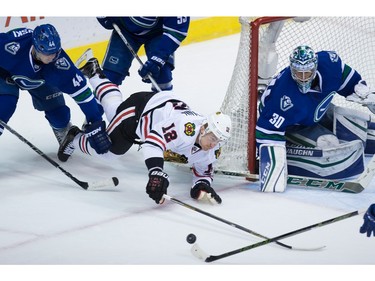 Chicago Blackhawks' Tomas Fleischmann, centre, of the Czech Republic, dives past Vancouver Canucks' Matt Bartkowski, left, to try and get to the puck in front of goalie Ryan Miller during the second period of an NHL hockey game in Vancouver, B.C., on Sunday March 27, 2016.