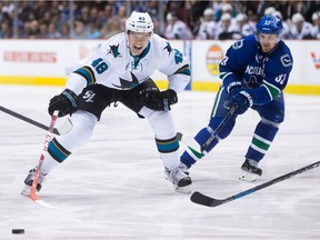 Tomas Hertl of the San Jose Sharks, left, reaches for the puck in front of Vancouver Canucks' captain Henrik Sedin during Tuesday's NHL game at Rogers Arena in Vancouver.