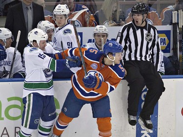 Vancouver Canucks ' Derek Dorsett (15) checks Edmonton Oilers' Mark Fayne (5) as the linesman jumps out of the way during second period NHL action in Edmonton, Alta., on Wednesday April 6, 2016. THE CANADIAN PRESS/Jason Franson