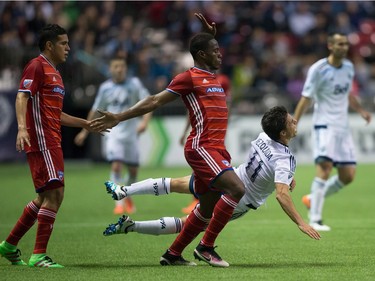 Vancouver Whitecaps' Nicolas Mezquida, right, is upended by FC Dallas' Maynor Figueroa, centre, during the second half of an MLS soccer game in Vancouver, B.C., on  April 23, 2016.