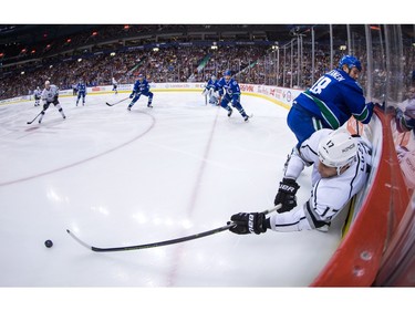 Los Angeles Kings' Milan Lucic, bottom right, passes the puck while being checked by Vancouver Canucks' Jake Virtanen during the first period of an NHL hockey game in Vancouver, B.C., on Monday April 4, 2016.