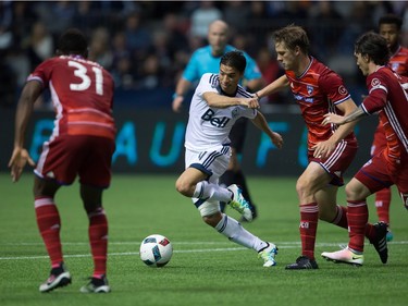 Vancouver Whitecaps' Nicolas Mezquida, centre, is held up by FC Dallas' Walker Zimmerman while moving with the ball during the second half in Vancouver on April 23, 2016.