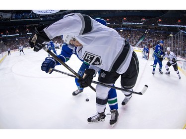 Los Angeles Kings' Trevor Lewis, centre, is checked by Vancouver Canucks' Matt Bartkowski, back, during the first period of an NHL hockey game in Vancouver, B.C., on Monday April 4, 2016.