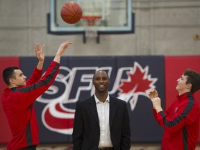 SFU's JJ Pankratz ( L ) tosses a basketball to teammate Matthew Rud ( R ) over the head of SFU men's basketball coach Virgil Hill ( C ). Hill has resigned after just one year