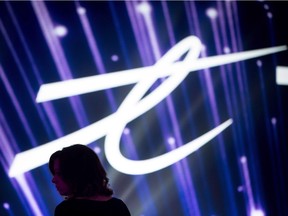 A woman is silhouetted as the Telus Corp. logo is displayed during a company event in Vancouver, B.C., on Friday October 2, 2015. Telus (TSX:T) has become the second Canadian telecommunications company to reach an agreement with the Competition Bureau over its participation in misleading premium text message services.