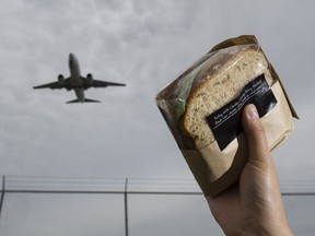A sandwich bought at YVR from a food vendor is held up below a landing WestJet plane in Richmond on Tuesday. WestJet says in excluding hot meals, they're able to continue offering low fares for passengers.