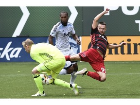 Vancouver Whitecaps goalkeeper David Ousted, left, steps in to grab the ball away from Portland Timbers forward Jack McInerney as Whitecaps defender Kendall Watson, centre, looks on Sunday in Portland, Ore. Waston was red-carded at the end of Vancouver's 4-2 loss.