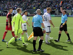 Referee Ted Unkel issues a red card to Vancouver Whitecaps defender Kendall Watson as defender Tim Parker (26) looks on.