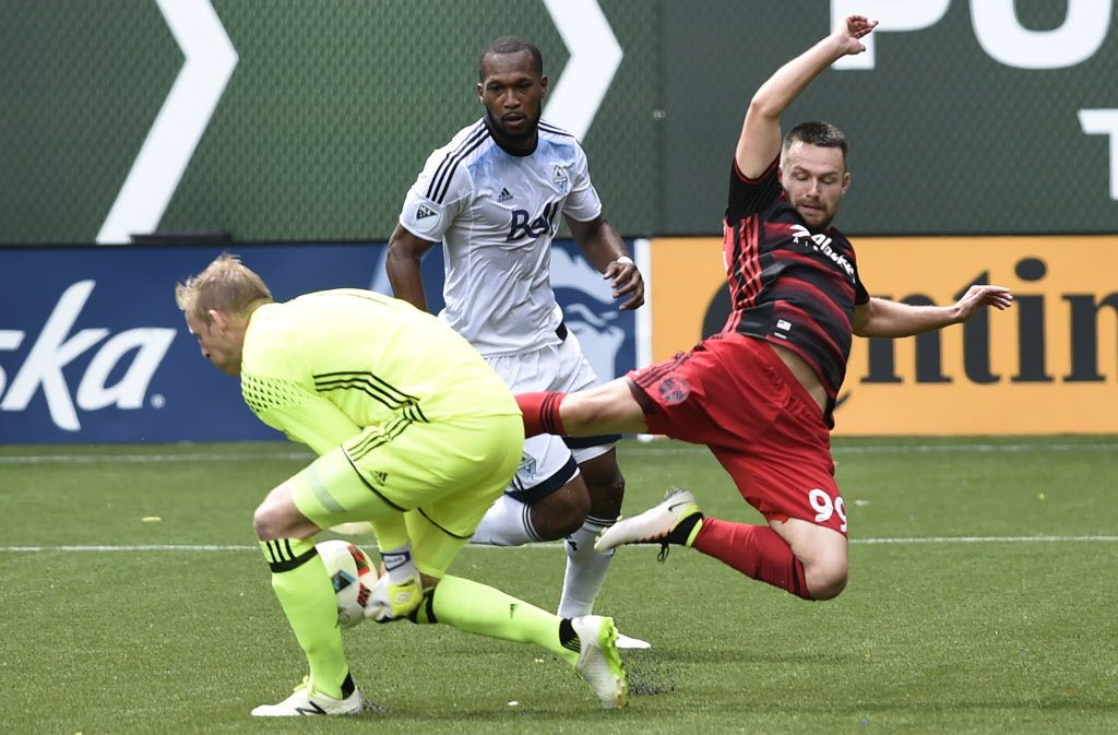 Vancouver Whitecaps goalkeeper David Ousted, left, steps in to grab the ball away from Portland Timbers forward Jack McInerney (99). 