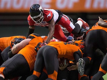 Calgary Stampeders' Osagie Odiase, top, leaps over the pile as B.C. Lions' quarterback Travis Lulay, bottom centre, rushes for a first down during the second half of a pre-season CFL football game in Vancouver, B.C., on Friday June 17, 2016. THE CANADIAN PRESS/Darryl Dyck ORG XMIT: VCRD125