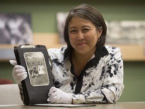 Carla Ayukawa poses for a photo as she holds a photo album open to a picture of her mother Michio and Uncle Kazoo at the Canadian War Museum Friday June 3, 2016 in Ottawa. Ayukawa donated the images showing life for Japanese people in internment camps to the museum.