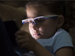 Liliya Sahiholnasab, 6, uses a special pair of glasses to help her correct her posture when using a tablet at her home in Richmond, B.C. Dr. Vahid Sahiholnasab has designed a pair of high-tech glasses to prevent children from developing bad posture while playing with devices like smartphones and video games.