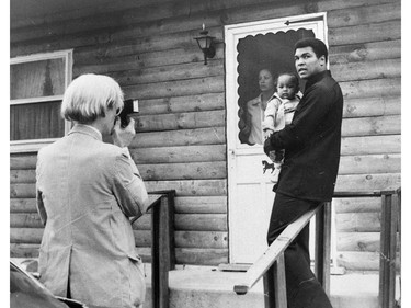 ADVANCE FOR USE SUNDAY, FEB. 23, 2014 AND THEREAFTER - FILE - In this Thursday, Aug. 18, 1977 file photo, artist Andy Warhol, left, photographs Muhammad Ali, his infant daughter, Hanna, and wife, Veronica, at Ali's training camp in Deer Lake, Pa. (AP Photo) ORG XMIT: NY355