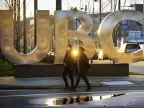 The UBC sign glows in the late evening light while students walk in around the campus.
