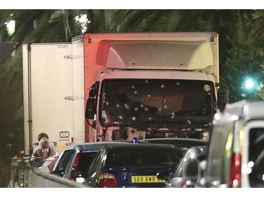 A policeman stands, watching the truck used for the attack near the scene of an attack after a truck drove onto the sidewalk late Thursday, and plowed through a crowd of revelers who gathered to watch the fireworks in the French resort city of Nice, southern France, Friday, July 15, 2016.