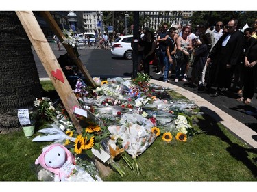 People stand on July 15, 2016 at a makeshift memorial near the site in Nice where a gunman smashed a truck into a crowd of revellers celebrating Bastille Day, killing at least 84 people. A gunman smashed a truck into a crowd of revellers celebrating Bastille Day in the French Riviera city of Nice, killing at least 84 people in what President Francois Hollande on July 15 called a "terrorist" attack.