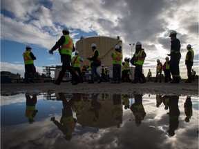File: Reporters and camera operators are reflected in a puddle while walking past a storage tank during a tour of FortisBC's existing Tilbury LNG facility in Delta, B.C., on October 21, 2014.