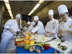 VCC Instructor John Lewis (left) speaks with culinary students, as they prepare their dishes during class at the downtown campus in Vancouver.