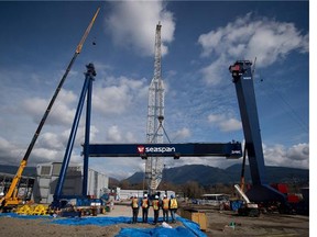 Workers watch as the main girder of a new 300-tonne gantry crane is lifted into place at Seaspan Vancouver Shipyards in North Vancouver, B.C., on Wednesday April 2, 2014.
