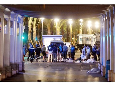 People stand next to covered bodies in the early hours of Friday, July 15, 2016, on the Promenade des Anglais in Nice, southern France.  France has been stunned again as a large white truck killed many people after it mowed through a crowd of revelers gathered for a Bastille Day fireworks display late Thursday evening, in the Riviera city of Nice.