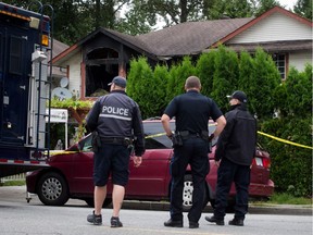 On Monday, police officers stand outside a Port Moody home where a woman was injured in a house fire Sunday and later died. A man cops believe to be her husband has been charged with second-degree murder and arson in the incident. — The Canadian Press files