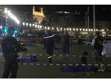 Soldiers, police officers and firefighters walk near dead bodies covered with a blue sheets on the Promenade des Anglais seafront in the French Riviera town of Nice on July 15, 2016, after a van drove into a crowd watching a fireworks display. At least 75 people were killed when a truck drove into a crowd watching a fireworks display in the French resort of Nice, a lawmaker said on July 15.