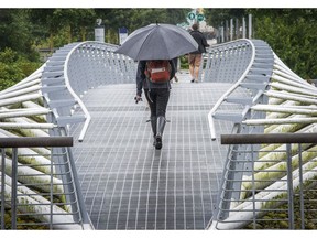 A lone pedestrian with an umbrella walks over the Canoe Bridge in Olympic Villiage Thursday July 7, 2016. Rain is dominating the 2016 summer weather patterns in Vancouver, B.C. putting a damper on festivals and outdoor activities.