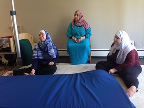 Sisters Hoda (left) and Maha Al-Sidawi from Syria examine a flooring mat brought by an occupational therapist on Saturday, Aug. 27, that they say will be more comfortable for them than sitting on carpet. Their mother, Fayza Al-Sidawi, sits between them.