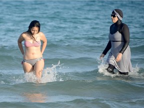 This file photo taken on August 16, 2016 shows Tunisian women, one (R) wearing a "burkini", a full-body swimsuit designed for Muslim women, walking in the water at Ghar El Melh beach near Bizerte, north-east of the capital Tunis.  The debate launched this summer in France over the Burkini is not causing such a stir in North Africa where the Islamic swimsuit is uncontroversial as the dress-code on the beaches has become increasingly prudish.