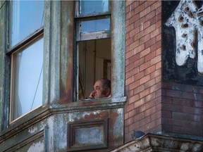 An elderly man looks out from an upper floor window at a single-room occupancy (SRO) hotel in Chinatown in Vancouver, B.C., on Thursday August 18, 2016.