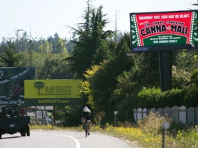 A cyclist rides by a large billboard on the Pat Bay Highway advertising the "Canna Mall," a collection of businesses targeting marijuana-buying customers.