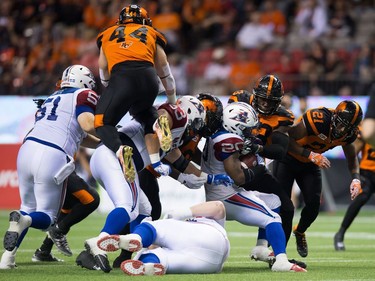 Montreal Alouettes' Tyrell Sutton (20) is tackled by B.C. Lions' Alex Bazzie, second right, as Adam Bighill (44) leaps above the crowd of players during the second half of a CFL football game in Vancouver, B.C., on Friday September 9, 2016.