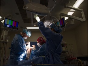 Dr. Darius Viskontas, left, with assistance from Dr. Anne Wachsmuth, centre, remove a cyst from a male patient's knee as Miwa Holm, an operating room registered nurse, adjusts a light at the Cambie Surgery Centre, in Vancouver on Wednesday, August 31, 2016. Dr. Brian Day, a self-styled champion of privatized health care, is bringing his fight to British Columbia Supreme Court on Tuesday for the start of a months-long trial he says is about patients' access to affordable treatment, while his opponents accuse him of trying to gut the core of Canada's medical system.