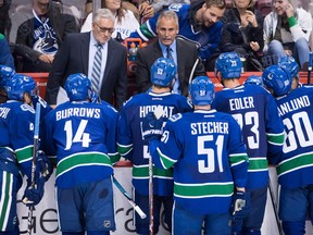 Vancouver Canucks' head coach Willie Desjardins, top right, speaks to his players as assistant coach Perry Pearn, top left, listens.