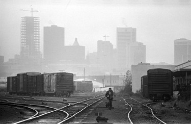 Man walking in Burlington-Northern freight yard with the misty city in the background. October 14, 1975.