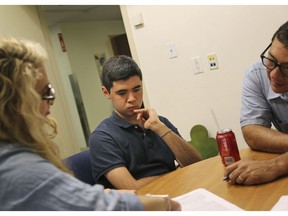 In this July 7, 2016, photo, Tom Bak, centre, looks on while his father, Tim Bak, right, talks with research coordinator Hillary Rieger at the Seaver Autism Center at Mount Sinai Hospital in New York. Tommy was diagnosed at age 3 with autism, after he stopped using words he'd learned months earlier and showed unusual behavior including repetitively lining up toys instead of playing with them.