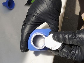 In this June 27, 2016 photo provided by the Royal Canadian Mounted Police, a member of the RCMP opens a printer ink bottle containing the opioid carfentanil imported from China, in Vancouver.