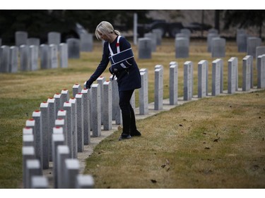 A woman places a poppy on a grave marker at a military cemetery following a Remembrance Day service in Calgary, Friday, Nov. 11, 2016.