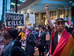 A young man draped in a rainbow flag raises his fist as he and other protesters hold a rally against U.S. President-elect Donald Trump outside the still under construction Trump Hotel, in Vancouver, B.C., on Thursday, November 10, 2016.