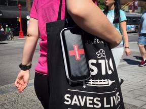 A woman carries a naloxone kit and a bag from Insite, the supervised injection site, while walking in the Downtown Eastside.