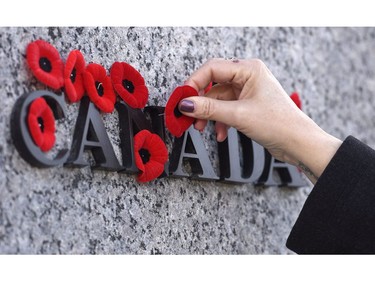 People place poppies over lettering in the National War Memorial during the National Remembrance Day ceremony, Friday, Nov. 11, 2016 in Ottawa.