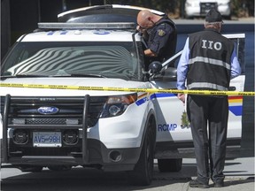 Am Independent Investigations Office investigator watches as an RCMP evidence specialist takes photos at a location where RCMP shot a man last year.