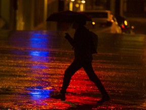 A pedestrian crosses the street on a rainy night in Vancouver.
